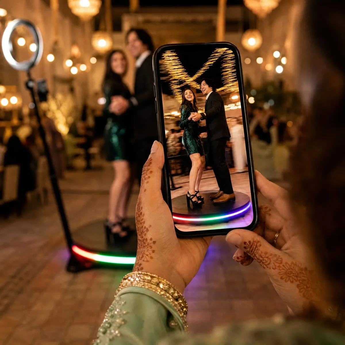 Sur l’écran d’un téléphone tenu à deux mains, l’image vidéo d’un couple qui tourne sur la plateforme du 360° ; la vraie plateforme et l’anneau lumineux, flous, derrière